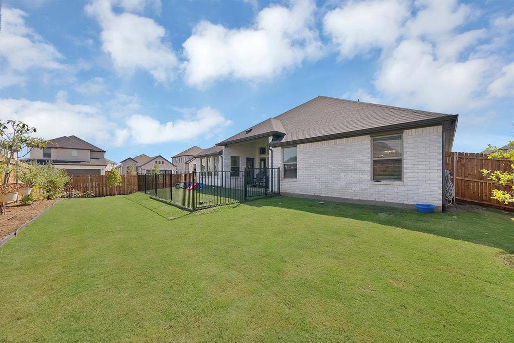 3701 Turpin Drive, Princeton, TX 75071 Expansive green lawn, white brick exterior, private wrought iron fenced area with artificial turf, brown wood perimeter fence, and professional landscaping that other homes do not have!