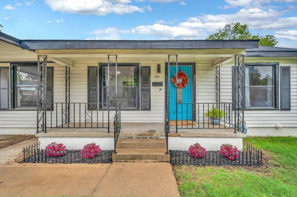 3720 Trice Avenue, Waco, TX 76707 Covered front porch with decorative wrought iron railings, white siding, black shutters, and a vibrant blue entry door