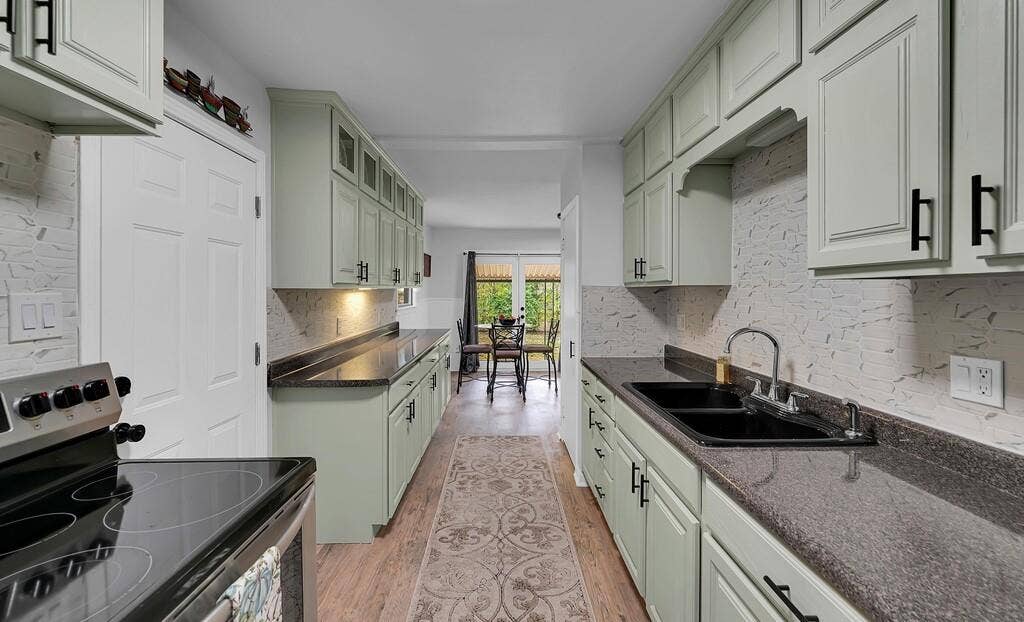 3720 Trice Avenue, Waco, TX 76707 Kitchen featuring wood-finish flooring, light green cabinetry with black hardware, dark countertops, and a white tiled backsplash
