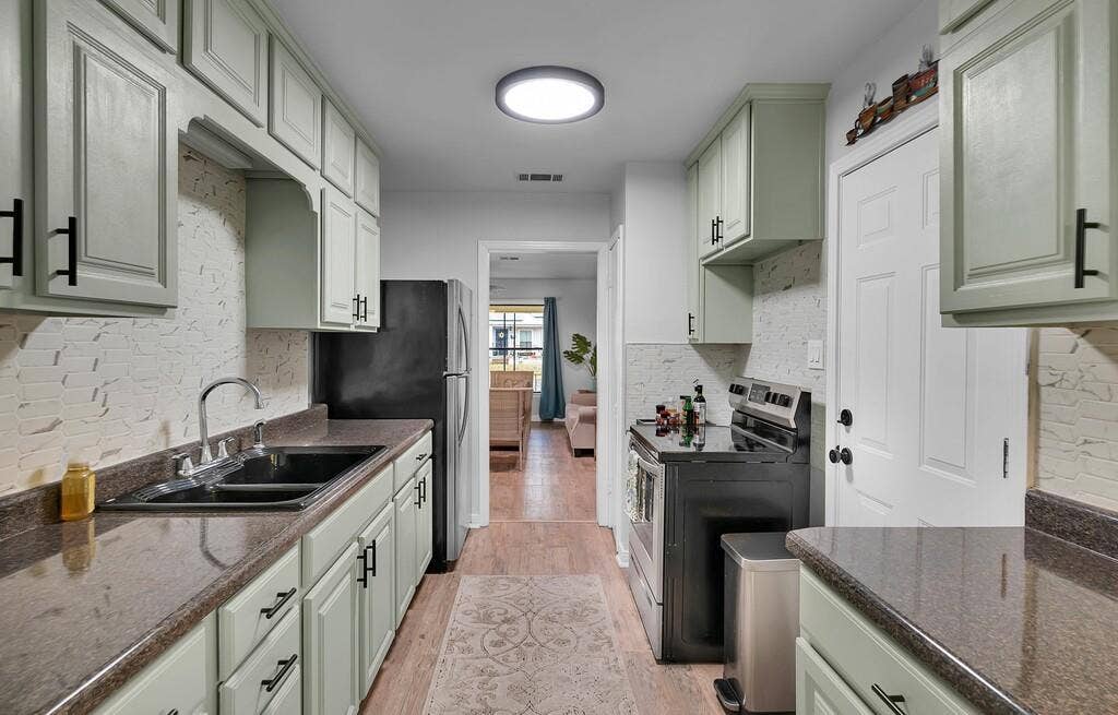 3720 Trice Avenue, Waco, TX 76707 Galley kitchen featuring light-toned cabinetry, dark countertops, a double basin sink, and a black appliance suite