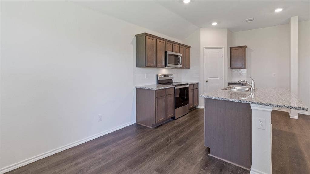 1117 Overhill Road, Josephine, TX 75135 Kitchen featuring wood-finish flooring, recessed lighting, stainless steel appliances, and a central island with a double basin sink and granite countertops