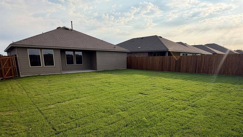 1117 Overhill Road, Josephine, TX 75135 Expansive green lawn with a privacy fence, concrete patio, and dark-framed windows