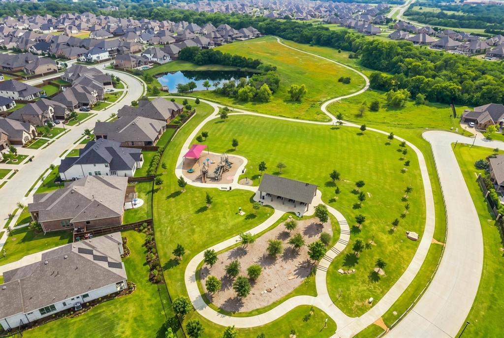 Expansive community green space featuring paved walking paths, a dedicated playground area, a central pond, and a covered pavilion