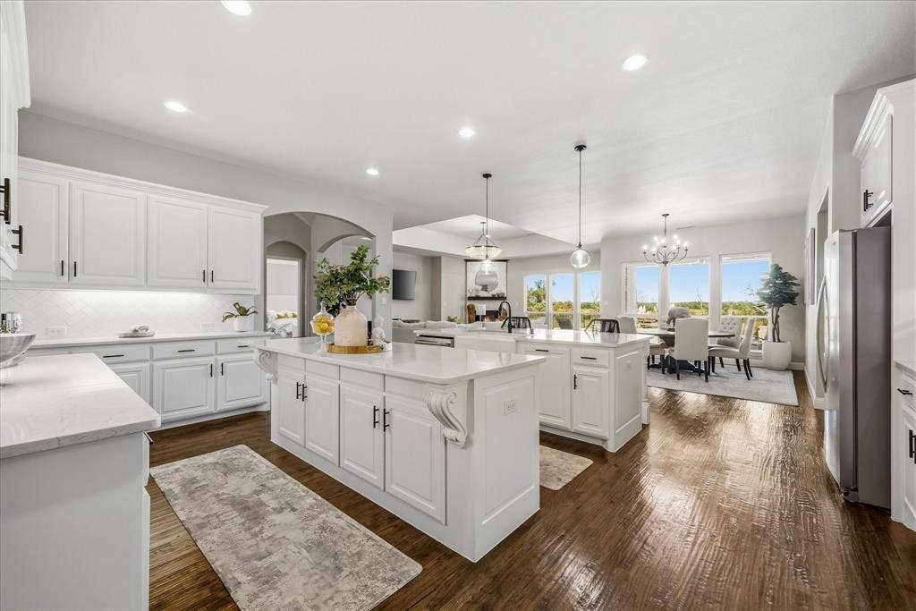 Spacious kitchen with dual islands, white cabinetry, integrated stainless steel appliances, and wood-finish flooring