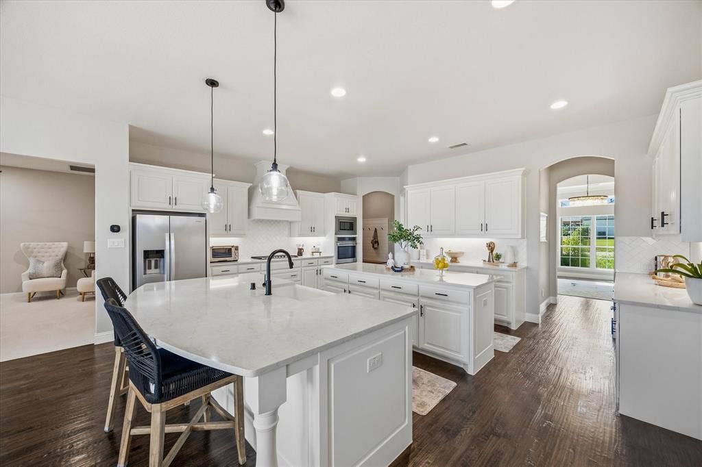 Kitchen featuring dark wood-finish flooring, white cabinetry, integrated stainless steel appliances, and two islands with light-colored countertops