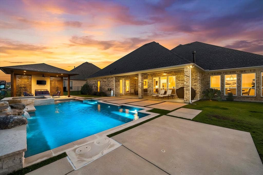 Brick exterior with multiple windows, covered patio, rectangular swimming pool with integrated spa, and an adjacent covered outdoor living structure