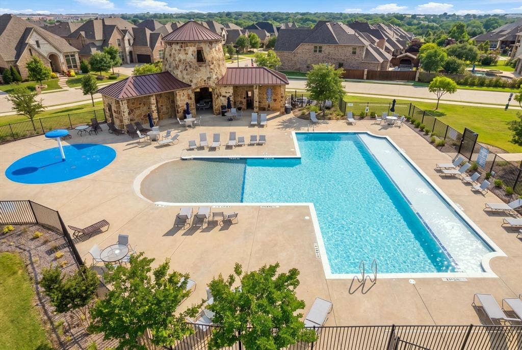 Expansive outdoor pool area featuring a large swimming pool, separate splash pad, and a stone-clad building with a covered patio