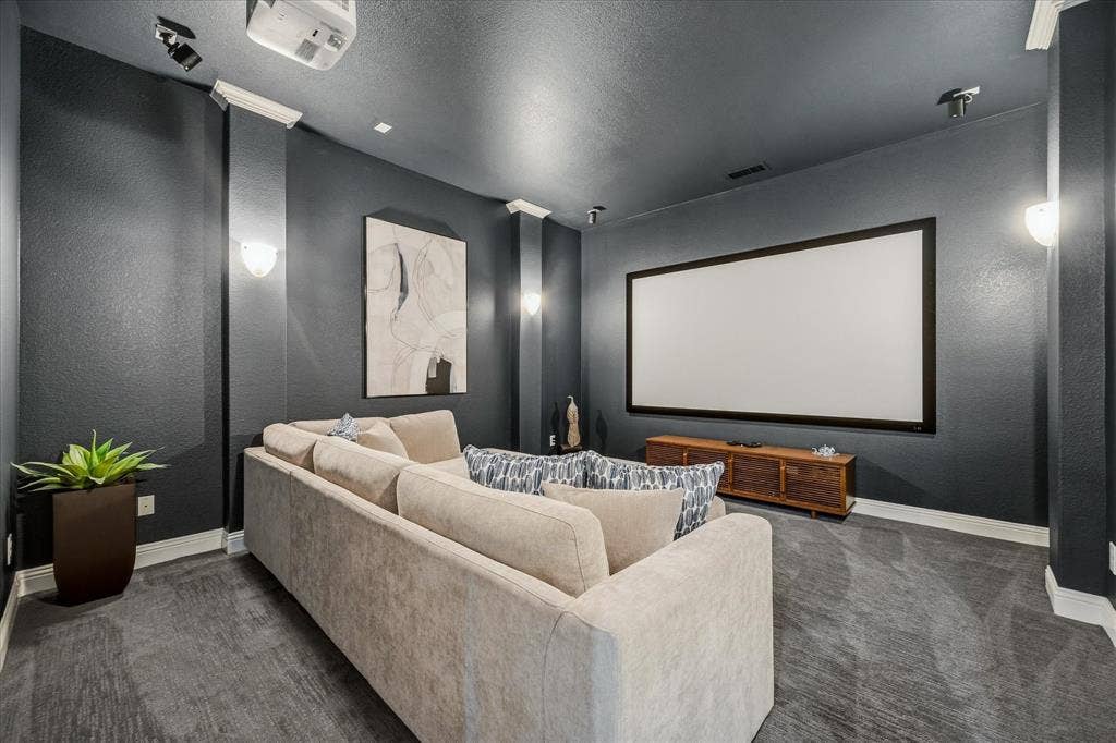 Dedicated media room featuring a large projection screen, mounted projector, recessed lighting, wall sconces, and a dark carpeted floor