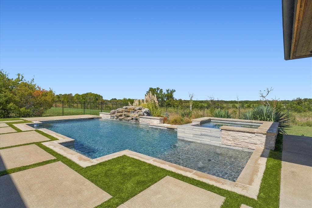 Expansive outdoor area featuring a swimming pool, integrated spa, rock waterfall, and large format concrete pavers with artificial turf accents