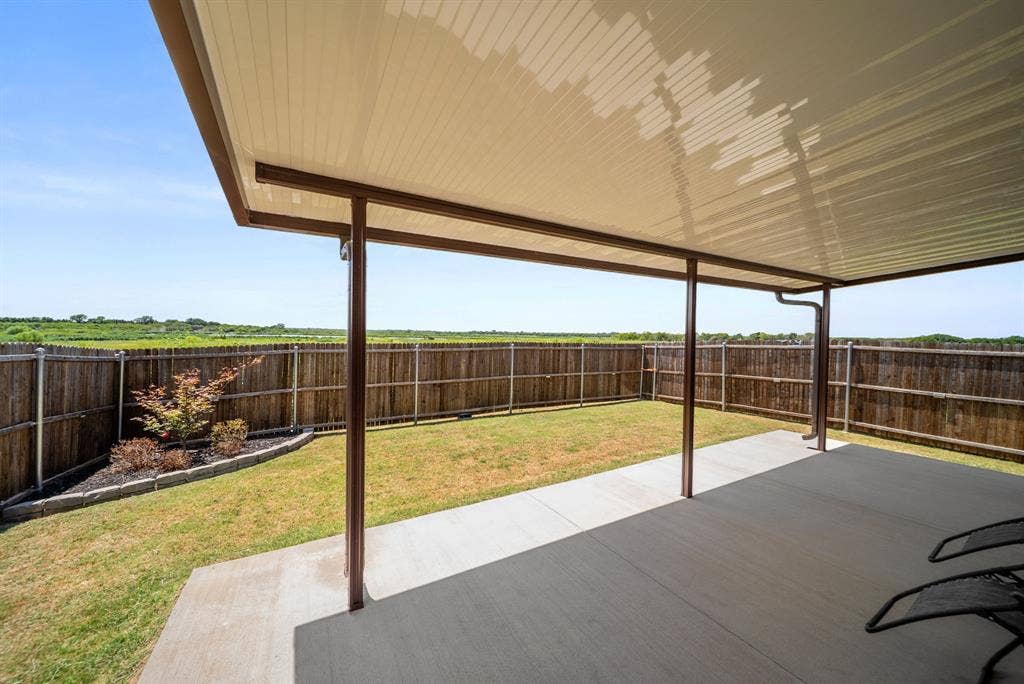 Expansive backyard featuring a covered patio, concrete walkway, and a wooden privacy fence