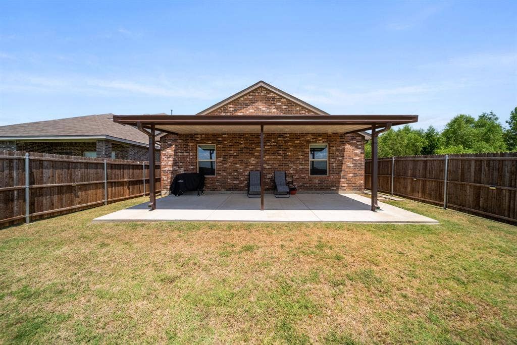 Expansive backyard featuring a covered patio, brick exterior, and wood fencing