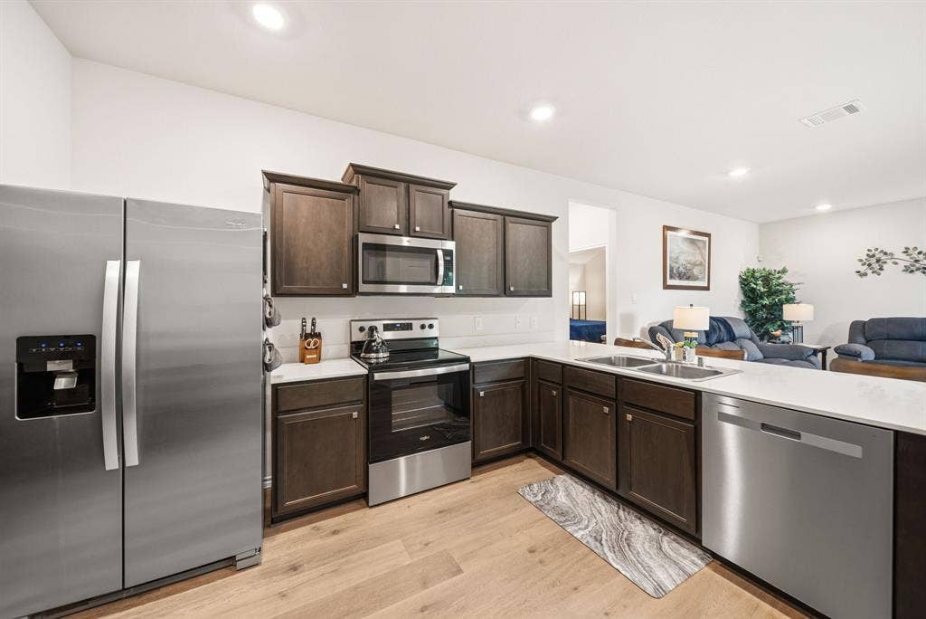 Kitchen featuring wood-finish flooring, dark wood cabinetry, stainless steel appliances, and solid surface countertops