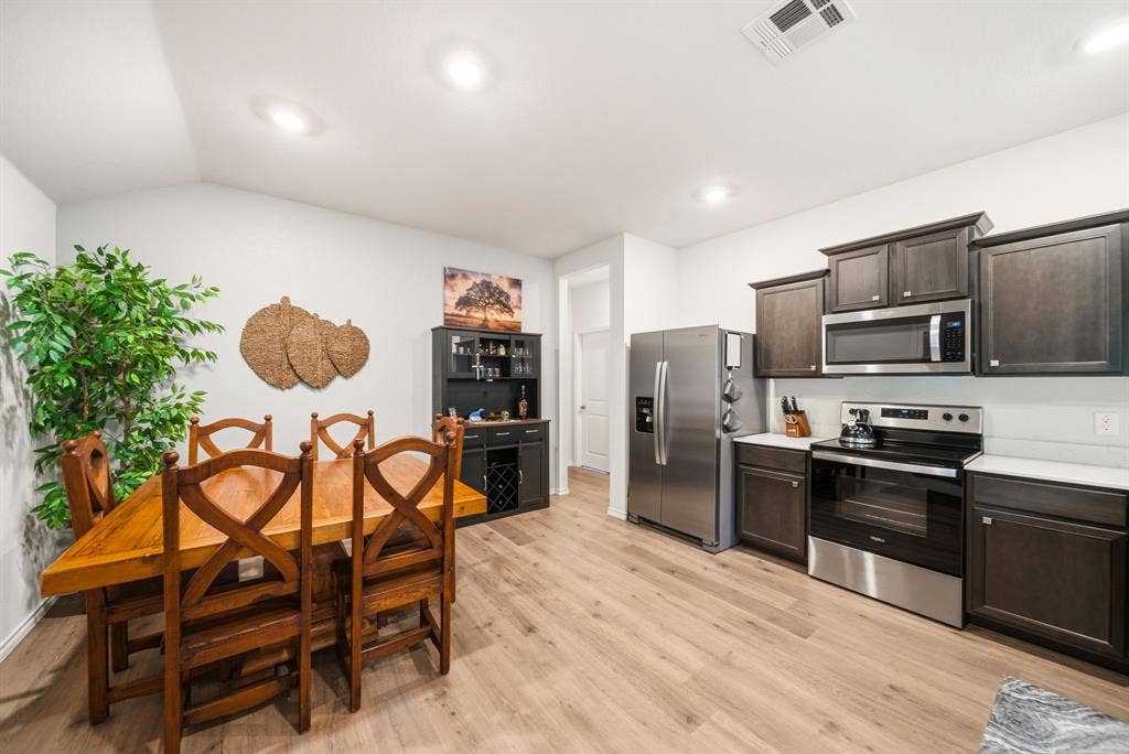 Open-concept living space with wood-finish flooring, recessed lighting, and a kitchen featuring stainless steel appliances, dark wood-finish cabinetry, and solid surface countertops