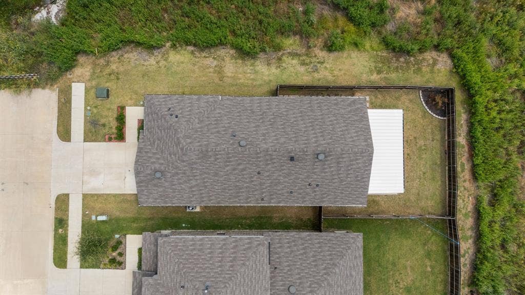 Gabled roofline with asphalt shingles, concrete driveway, concrete walkways, wood fencing, and a white metal roof structure