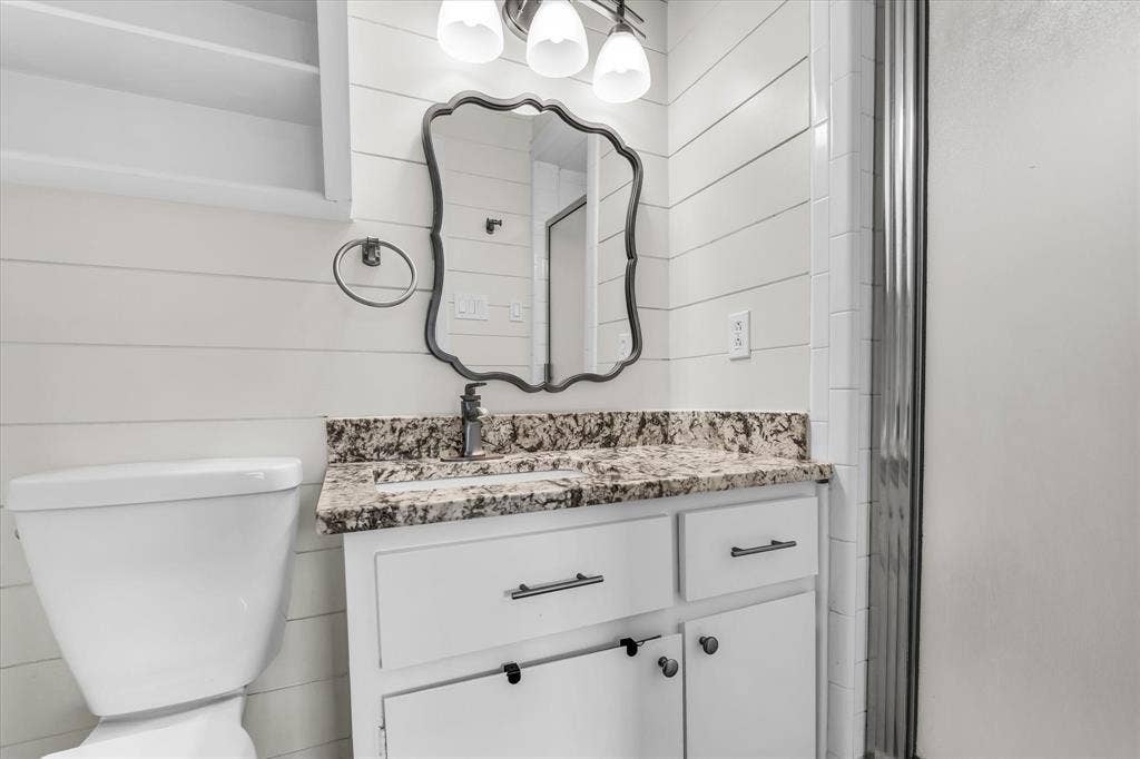 1214 Baylor Avenue, #109, Waco, TX 76706 White shiplap walls, vanity with granite countertop, white cabinetry with dark hardware, framed mirror, and a modern light fixture