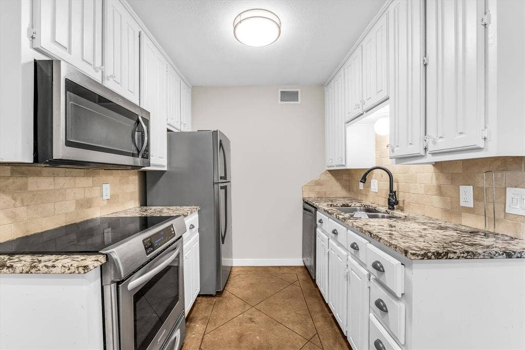 1214 Baylor Avenue, #109, Waco, TX 76706 White cabinetry, stainless steel appliances, granite-look countertops, tiled backsplash, and a matte black faucet
