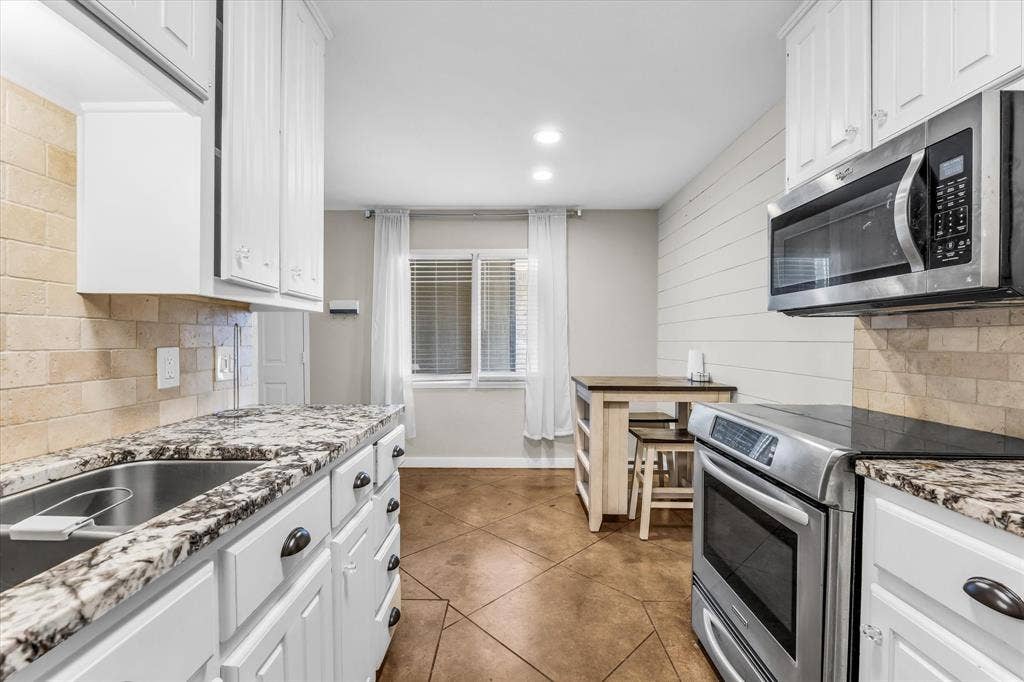 1214 Baylor Avenue, #109, Waco, TX 76706 White cabinetry, granite-finish countertops, stainless steel appliances, brick-patterned tile backsplash, and wood-finish flooring