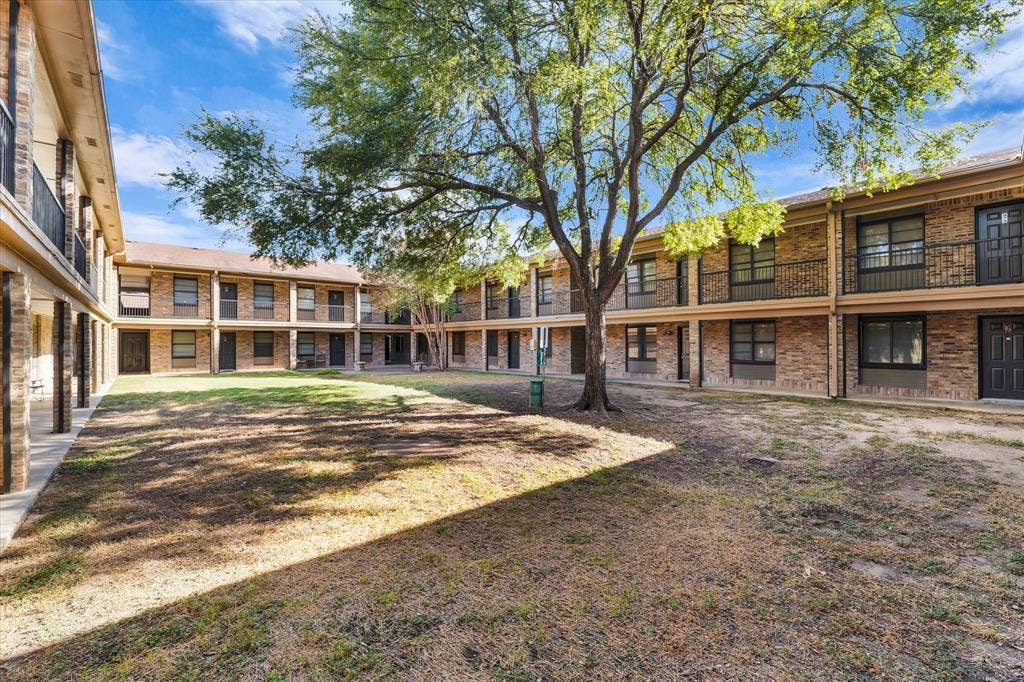 1214 Baylor Avenue, #109, Waco, TX 76706 Central courtyard featuring a mature tree, surrounding two-story buildings with brick exteriors, and upper-level balconies with wrought iron railings