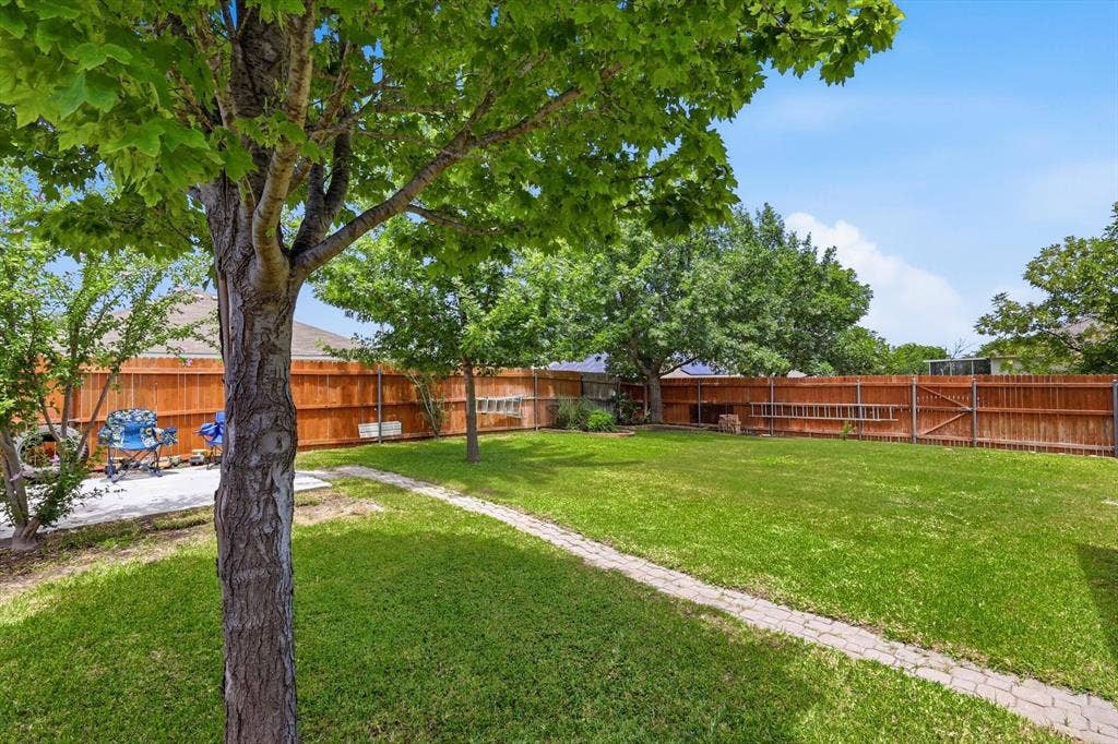 800 Poncho Lane, Fort Worth, TX 76052 Expansive backyard featuring a mature shade tree, manicured lawn, wooden privacy fencing, and defined landscape pathways