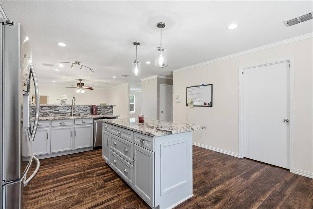 800 Poncho Lane, Fort Worth, TX 76052 Renovated kitchen featuring white cabinetry, a large center island with granite countertops, stainless steel appliances, wood-finish flooring, and pendant lighting
