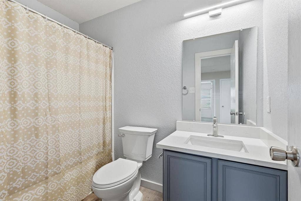 800 Poncho Lane, Fort Worth, TX 76052 Modern bathroom featuring a dark blue vanity with white countertop and rectangular vessel sink, brushed nickel faucet, large framed mirror with integrated lighting, and a patterned shower curtain with coordinating tile surround