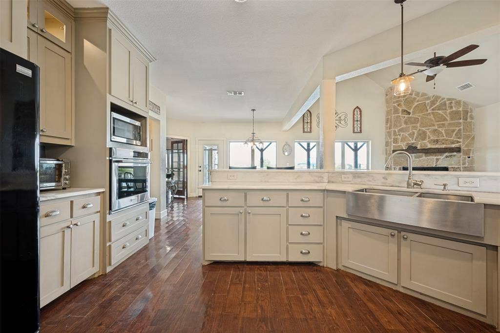 8400 Holder Road, Northlake, TX 76247 Kitchen featuring wood-finish flooring, light-colored cabinetry, stainless steel appliances, a farmhouse sink, and stone accent wall