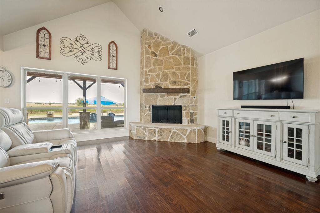 8400 Holder Road, Northlake, TX 76247 Vaulted ceiling, stone-clad wood burning fireplace with wood mantle, dark wood-finish flooring, and large windows overlooking an outdoor pool