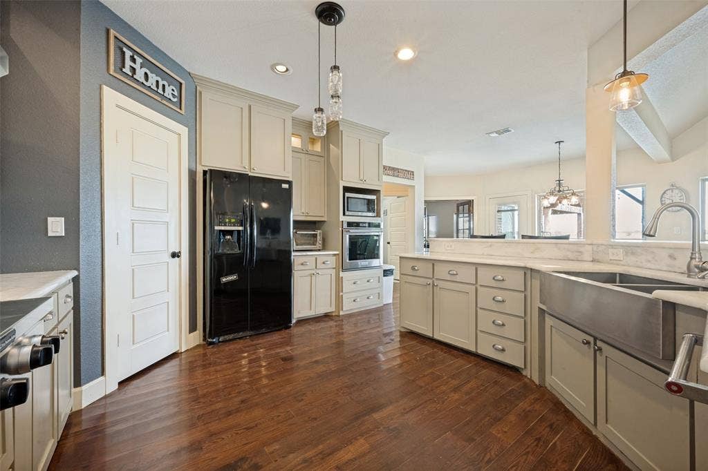 8400 Holder Road, Northlake, TX 76247 Spacious kitchen featuring cream cabinetry, stainless steel appliances including a double wall oven and side-by-side refrigerator, wood-finish flooring, and a large center island with sink and prep space