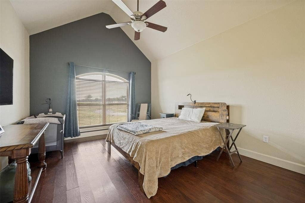 8400 Holder Road, Northlake, TX 76247 Vaulted ceiling with a ceiling fan, arched window with horizontal blinds, wood-finish flooring, and a contrasting accent wall