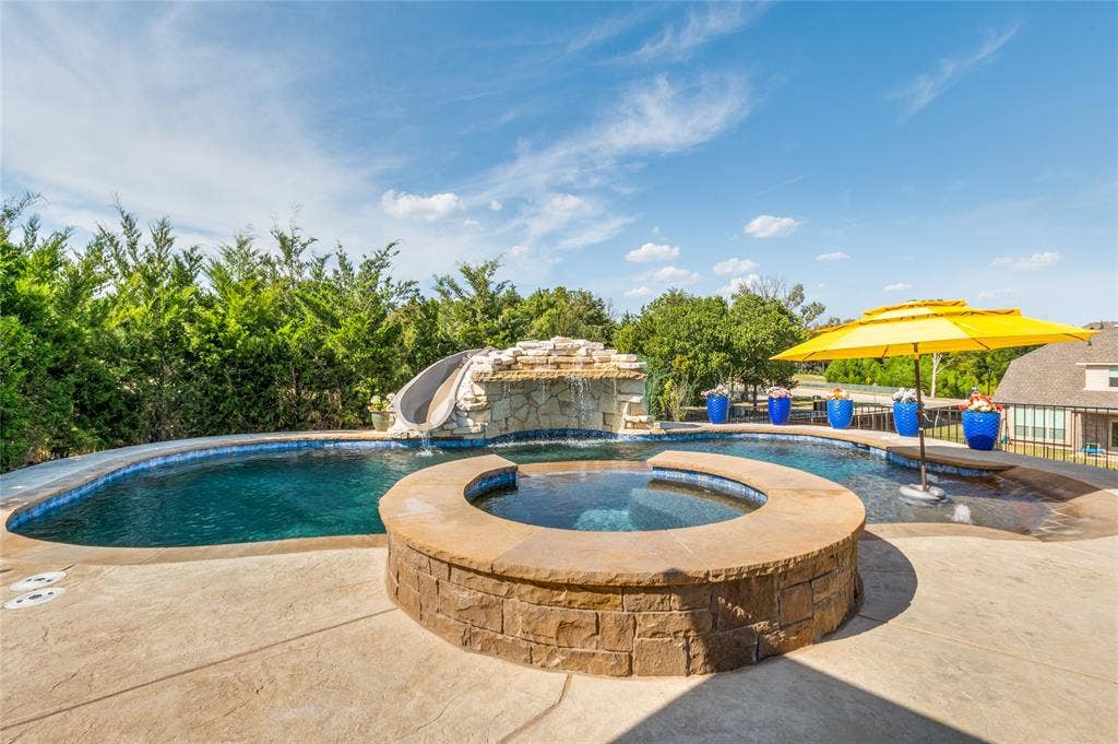 4601 Massey Meadows Way, Midlothian, TX 76065 Resort-style pool with a rock waterfall feature, built-in spa, integrated slide, and extensive stamped concrete patio