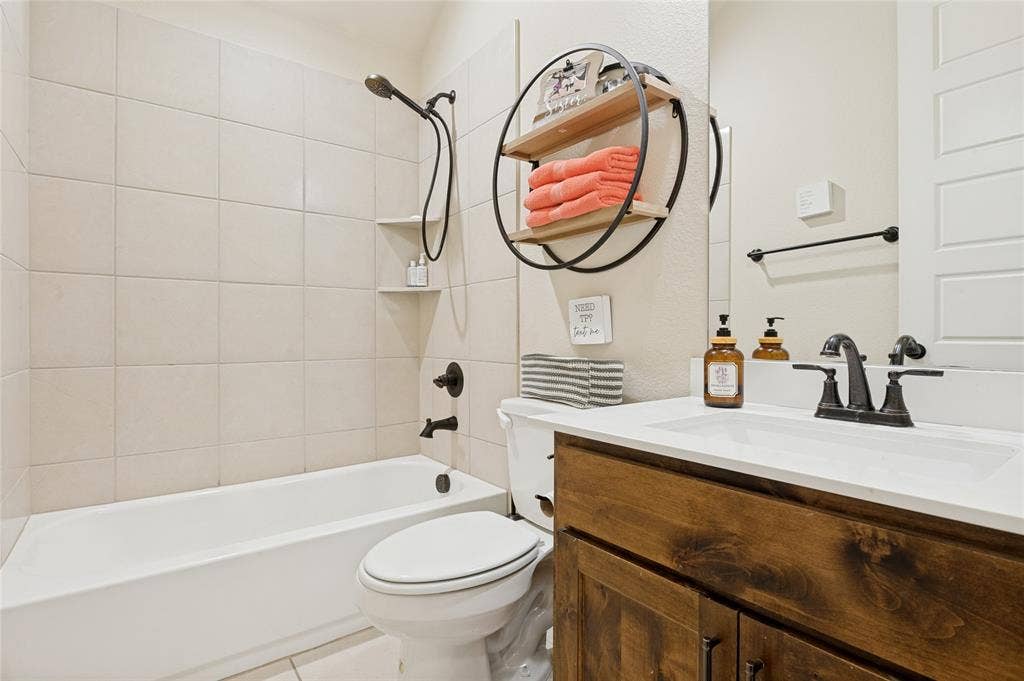 4601 Massey Meadows Way, Midlothian, TX 76065 Built-in tub with ceramic tile surround, recessed shower niche, wood-finish vanity with countertop, and integrated sink
