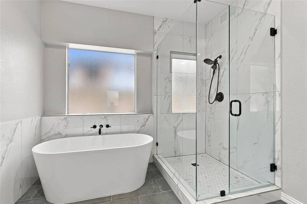 1820 Forest Bend Lane, Keller, TX 76248 Freestanding soaking tub with wall-mounted matte black fixtures, marble-look tile surround, and a glass-enclosed shower with hexagon tile floor.
