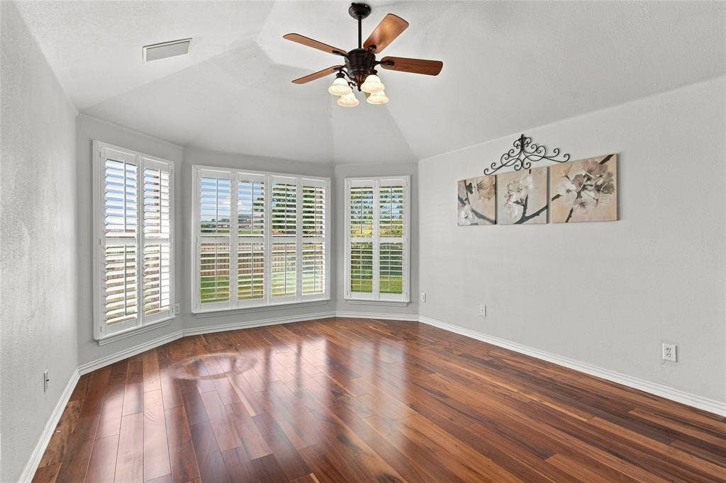 1820 Forest Bend Lane, Keller, TX 76248 Primary bedroom with bay window with plantation shutters, vaulted ceiling, wood-finish flooring, and a ceiling fan with integrated lighting