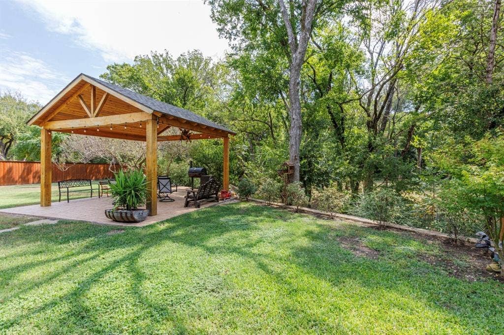 1408 Quapaw Trail, Mesquite, TX 75149 Expansive green lawn featuring a wood-framed outdoor pavilion with a shingled roof, string lighting, and a paved patio area