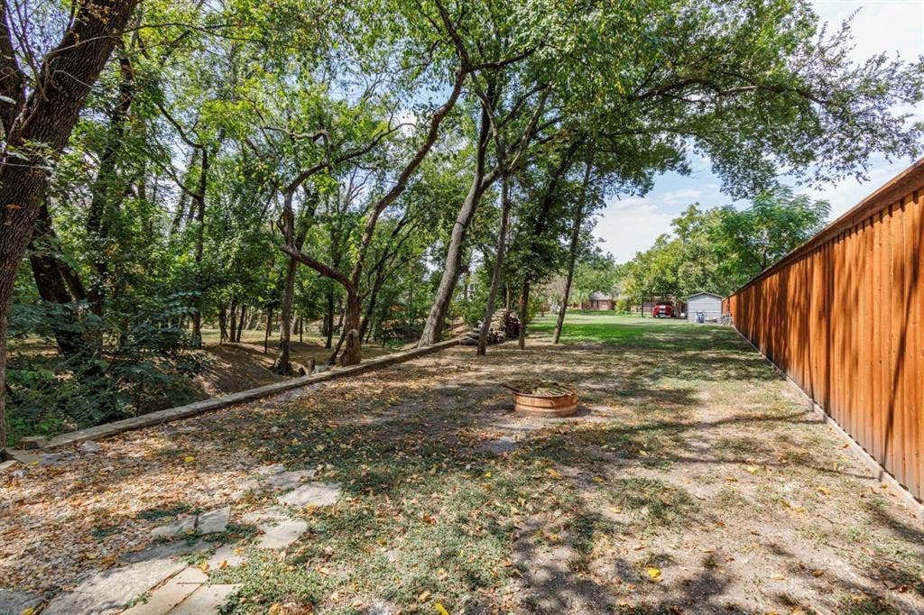 1408 Quapaw Trail, Mesquite, TX 75149 Expansive backyard featuring a wood fence, mature trees, and a fire pit