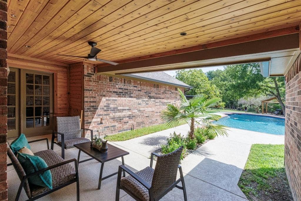 1408 Quapaw Trail, Mesquite, TX 75149 Covered patio with wood-finish ceiling and ceiling fan overlooking sparkling in-ground swimming pool, mature landscaping with tropical plantings, and expansive concrete decking