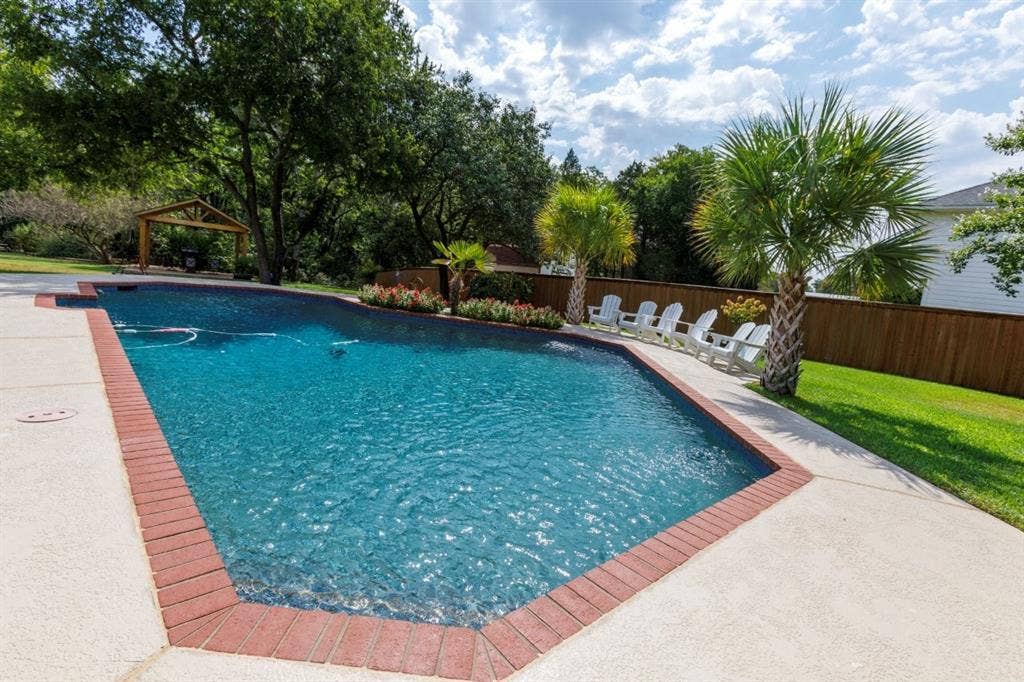 1408 Quapaw Trail, Mesquite, TX 75149 Swimming pool with a brick coping, an expansive concrete deck, mature palm trees, and a wooden privacy fence