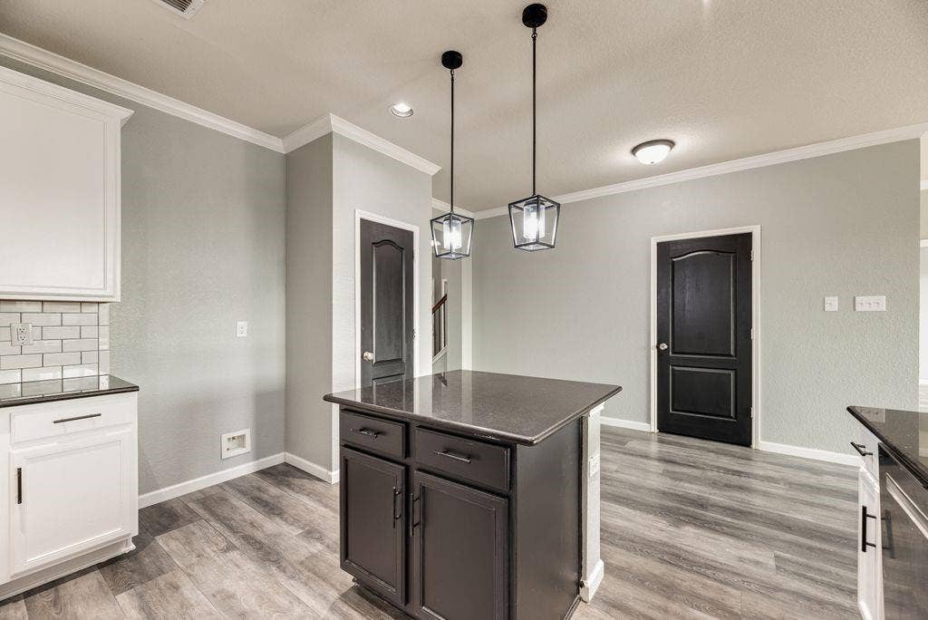 259 Saddlebrook Lane, Waxahachie, TX 75165 Modern kitchen and dining area featuring a dark-stained island with storage cabinetry, wood-finish flooring throughout, and pendant lighting with glass shades