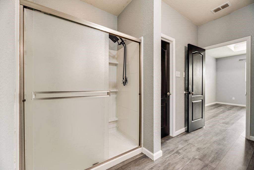 259 Saddlebrook Lane, Waxahachie, TX 75165 Primary bathroom featuring a frameless glass-enclosed walk-in shower with chrome fixtures, white subway tile surround, and polished wood-finish flooring