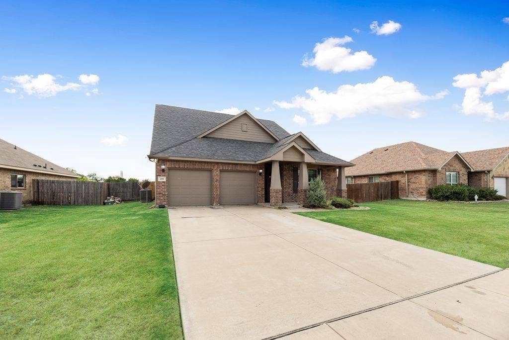 259 Saddlebrook Lane, Waxahachie, TX 75165 Brick exterior with a gabled roofline, two-car garage, covered porch entry, and a concrete driveway