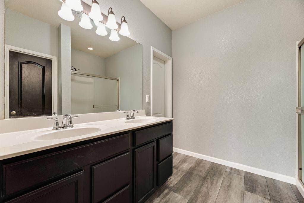 259 Saddlebrook Lane, Waxahachie, TX 75165 Dual-vanity bathroom featuring a long white quartz countertop, dark cabinetry with multiple drawers, polished chrome faucets, an expansive framed mirror, and contemporary wall-mounted lighting fixtures