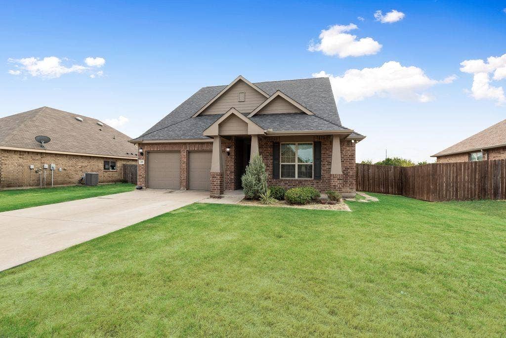 259 Saddlebrook Lane, Waxahachie, TX 75165 Brick exterior with gabled roof lines, attached two-car garage, concrete driveway, and front landscaping