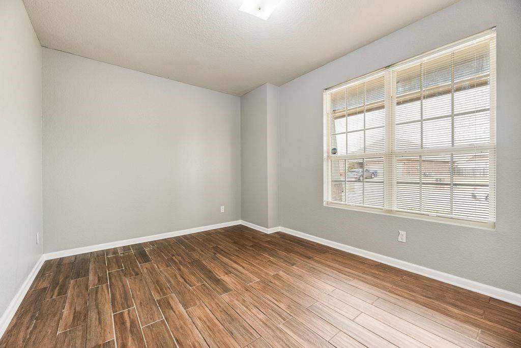 259 Saddlebrook Lane, Waxahachie, TX 75165 Bright, light-filled bedroom featuring gleaming wood-finish flooring, neutral wall finishes, and expansive gridded windows with interior shutters providing natural illumination and privacy control