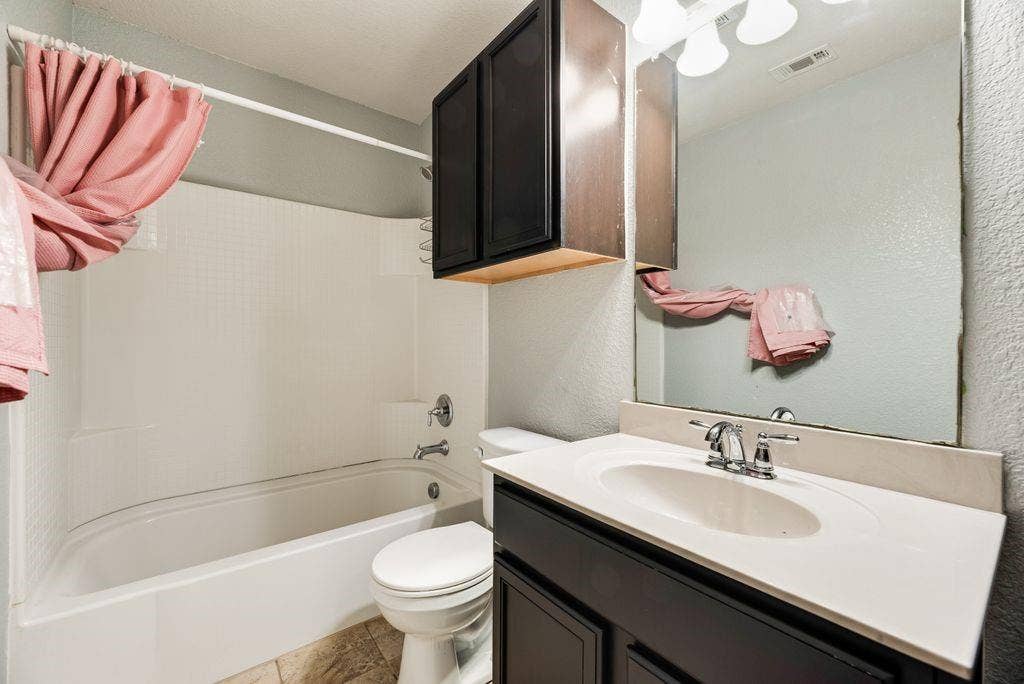 259 Saddlebrook Lane, Waxahachie, TX 75165 Spa-inspired bathroom featuring a vanity with white quartz countertop and matte black hardware, a large frameless mirror, dark cabinetry with wood-finish accents, ceramic tile surround, and an integrated bathtub-shower combination with tile surround and chrome fixtures