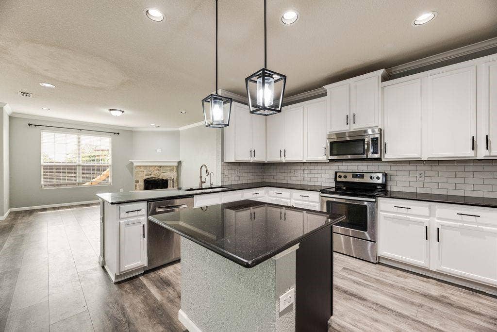 259 Saddlebrook Lane, Waxahachie, TX 75165 Modern kitchen featuring white cabinetry with chrome hardware, stainless steel appliances, a black quartz island countertop with waterfall edge, subway tile backsplash, recessed and pendant lighting, and wood-finish flooring throughout the open layout