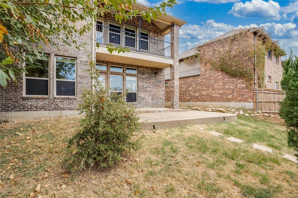 1014 Kaylie Street, Grand Prairie, TX 75052 Brick exterior featuring multiple windows, an upper-level balcony with metal railing, and a ground-level concrete patio