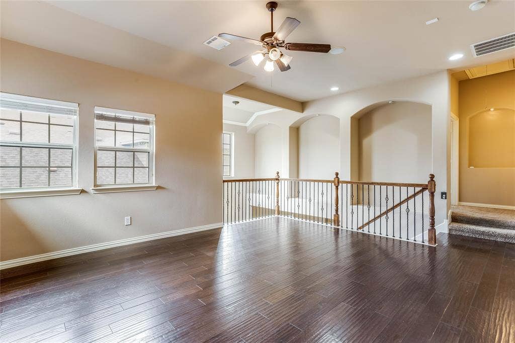 1014 Kaylie Street, Grand Prairie, TX 75052 Dark wood-finish flooring, two large windows, a ceiling fan with integrated lighting, a wood and iron railing, and arched wall niches