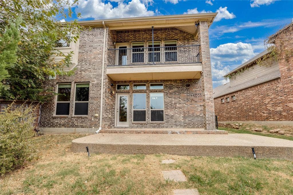 1014 Kaylie Street, Grand Prairie, TX 75052 Brick exterior with multiple windows, a second-story balcony with metal railing, and a ground-level concrete patio