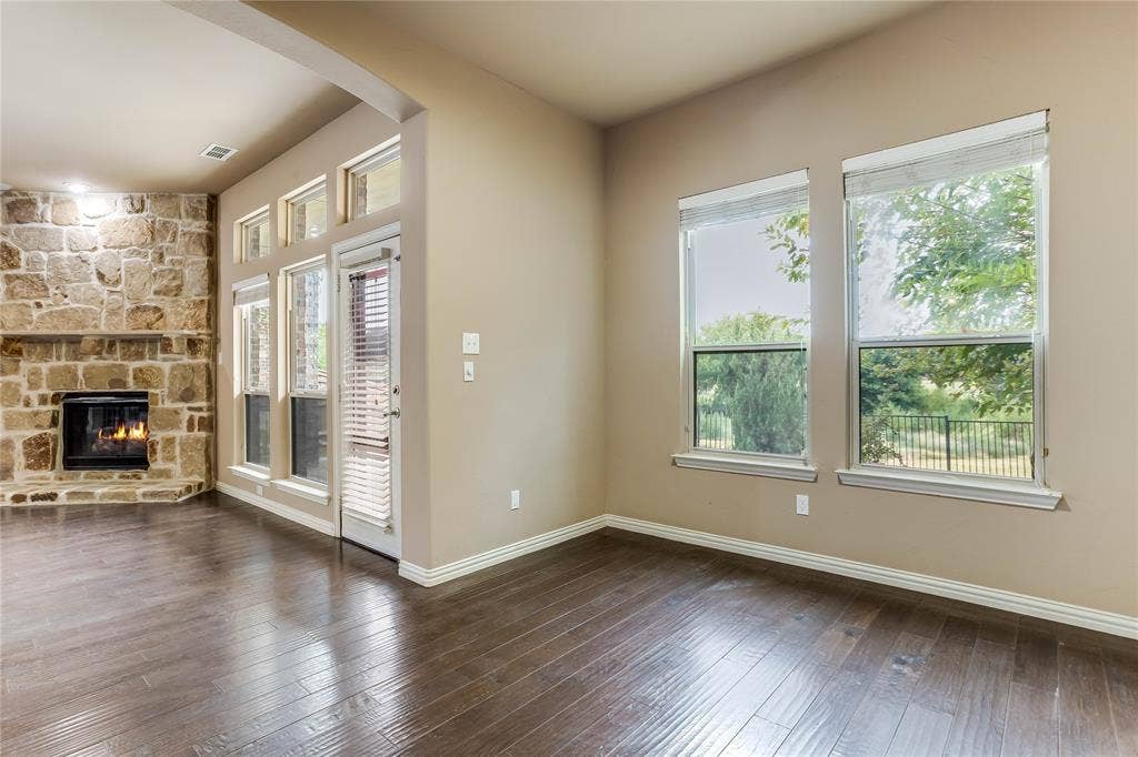 1014 Kaylie Street, Grand Prairie, TX 75052 Stone-clad fireplace, wood-finish flooring, multiple large windows, transom window detailing, and an exterior door with integrated blinds