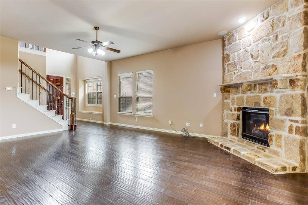 1014 Kaylie Street, Grand Prairie, TX 75052 Stone-clad fireplace with hearth, dark wood-finish flooring, staircase with dark wood handrail and iron balusters, recessed lighting, and ceiling fan with integrated lighting